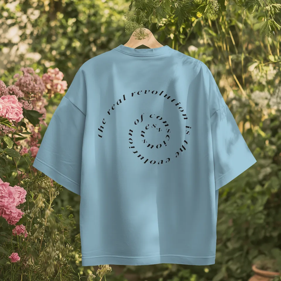 Back of the Rare Blue Consciousness t-shirt with the spiral text print, hanging in a garden
